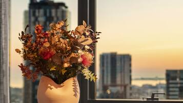 A round table with a vase of flowers, two chairs, and a view of a cityscape through a large window.