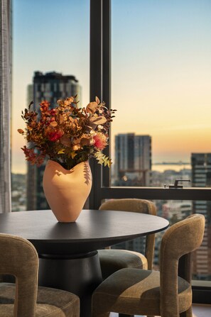 Una mesa redonda con un jarrón de flores, dos sillas y vistas a un paisaje urbano a través de un ventanal grande.
