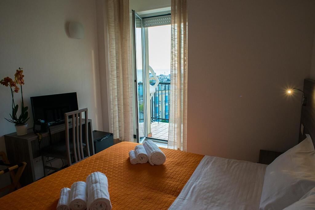 A hotel room with a bed, a desk with a TV, a chair, and a view of the outside.