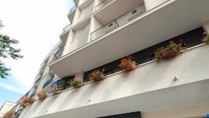 Ein mehrstöckiges Gebäude mit flacher Fassade, Balkonen mit Blumenkästen und einem sichtbaren Schaufenster mit dem Schriftzug 'MADISON'.
