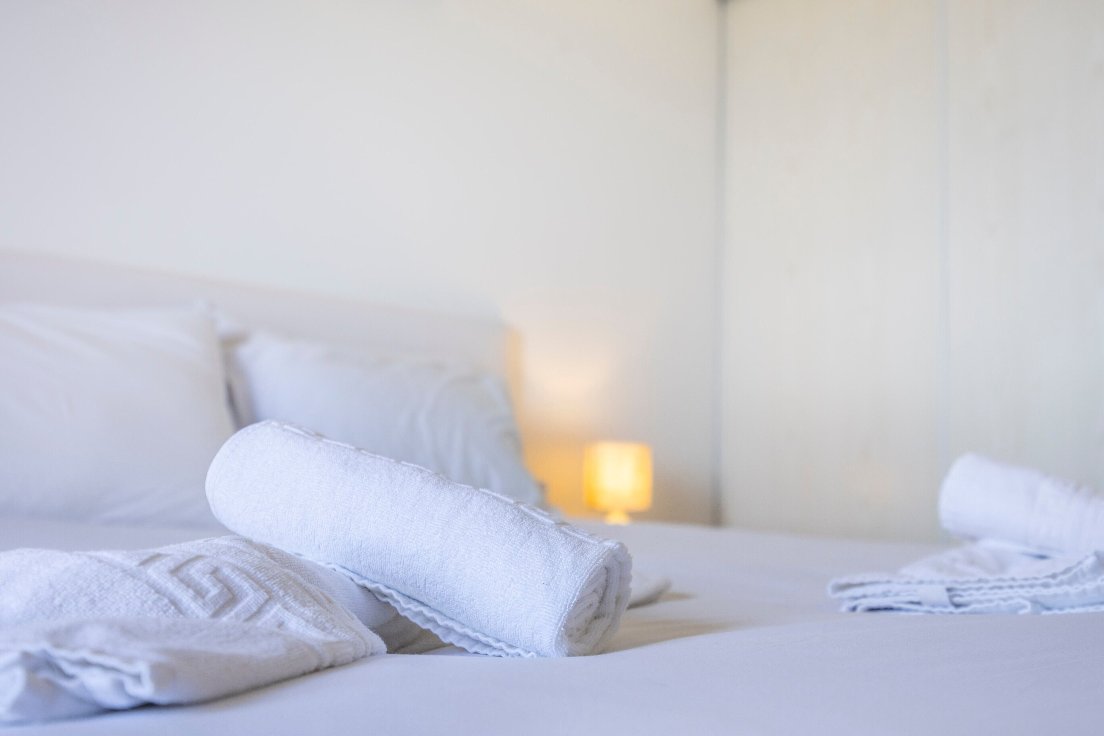 A neatly made bed with rolled white towels and a lamp in the background.