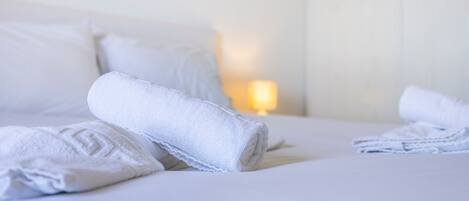 A neatly made bed with rolled white towels and a lamp in the background.