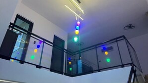 Un interior moderno con barandilla de vidrio, una escalera y una lámpara de techo con múltiples bombillas de colores.