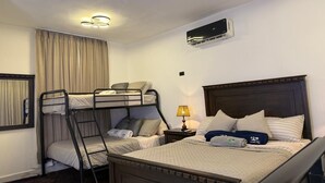 Habitación de hotel con literas, una mesita de noche con lámpara, un aire acondicionado y una ventana con cortinas.