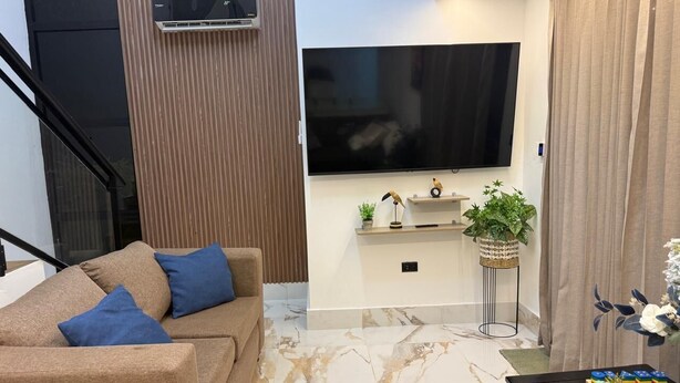Una sala de estar moderna con un sofá, un televisor de pantalla plana, una mesita con objetos decorativos y una planta en maceta.