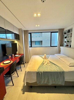 Ein Hotelzimmer mit Bett, Schreibtisch mit Stuhl, Fernseher und Fenster mit Blick auf Gebäude.