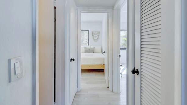 Ein Flur, der in ein Schlafzimmer mit Bett, Lichtschalter und Deckenleuchte führt.