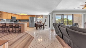 A modern kitchen with a central island, bar stools, and a dining area with a table and chairs. - Sea Club #42 - Stellar Escape (Indian Shores)