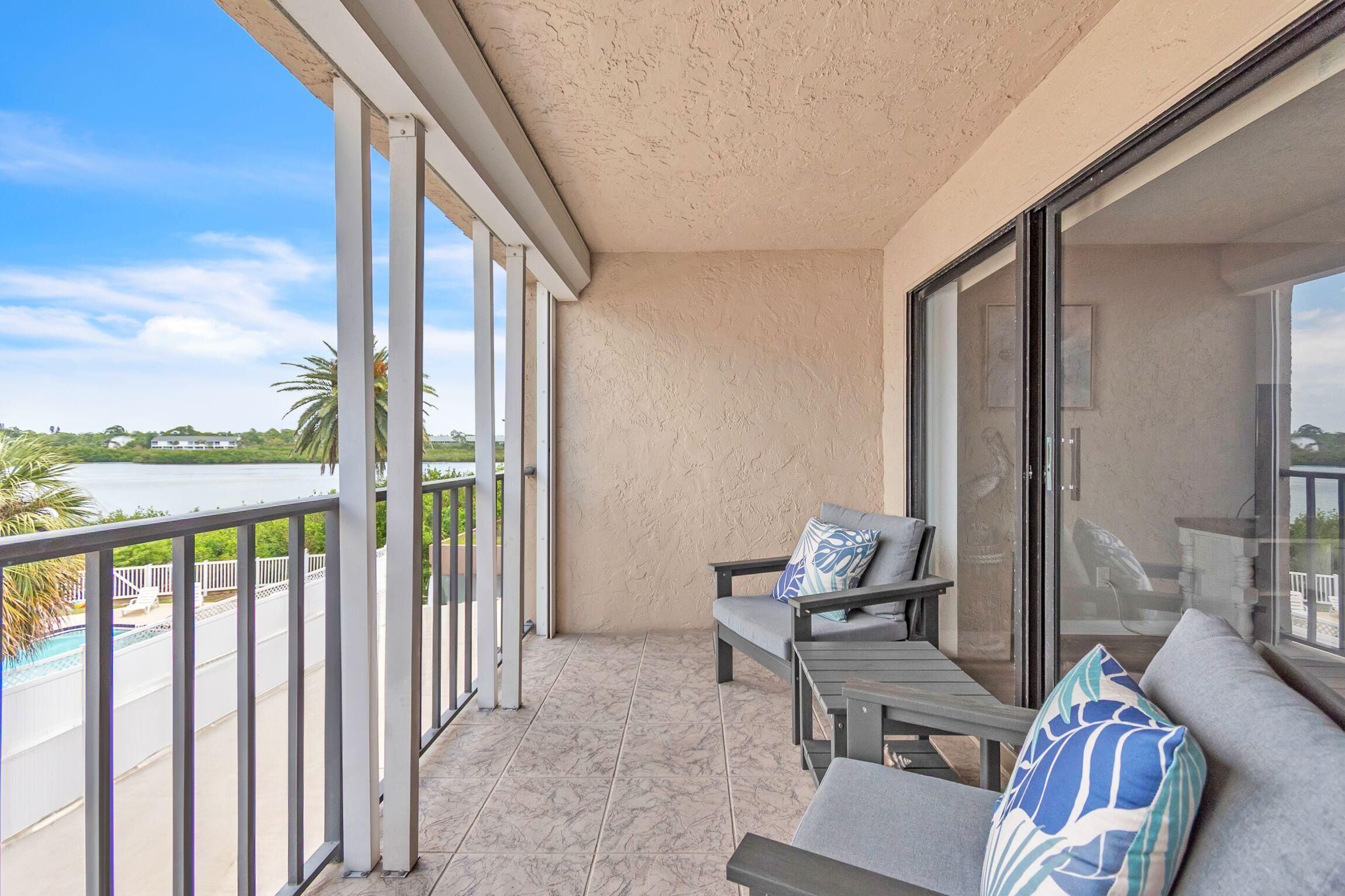 A balcony with a view of a body of water, a pool, and palm trees.
