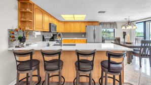 A modern kitchen with a central island, bar stools, and a dining area with chairs. - Sea Club #42 - Stellar Escape (Indian Shores)