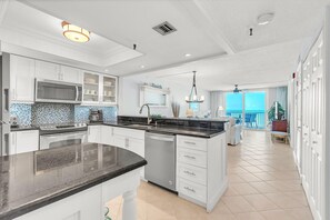 A modern kitchen with white cabinetry, a large island, and a view to the living area. - Sand Castle II #2603 - Premier (Indian Shores)