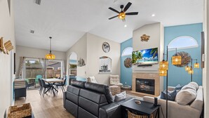 Un salon moderne avec une cheminée, un coin repas et une cuisine en arrière-plan.