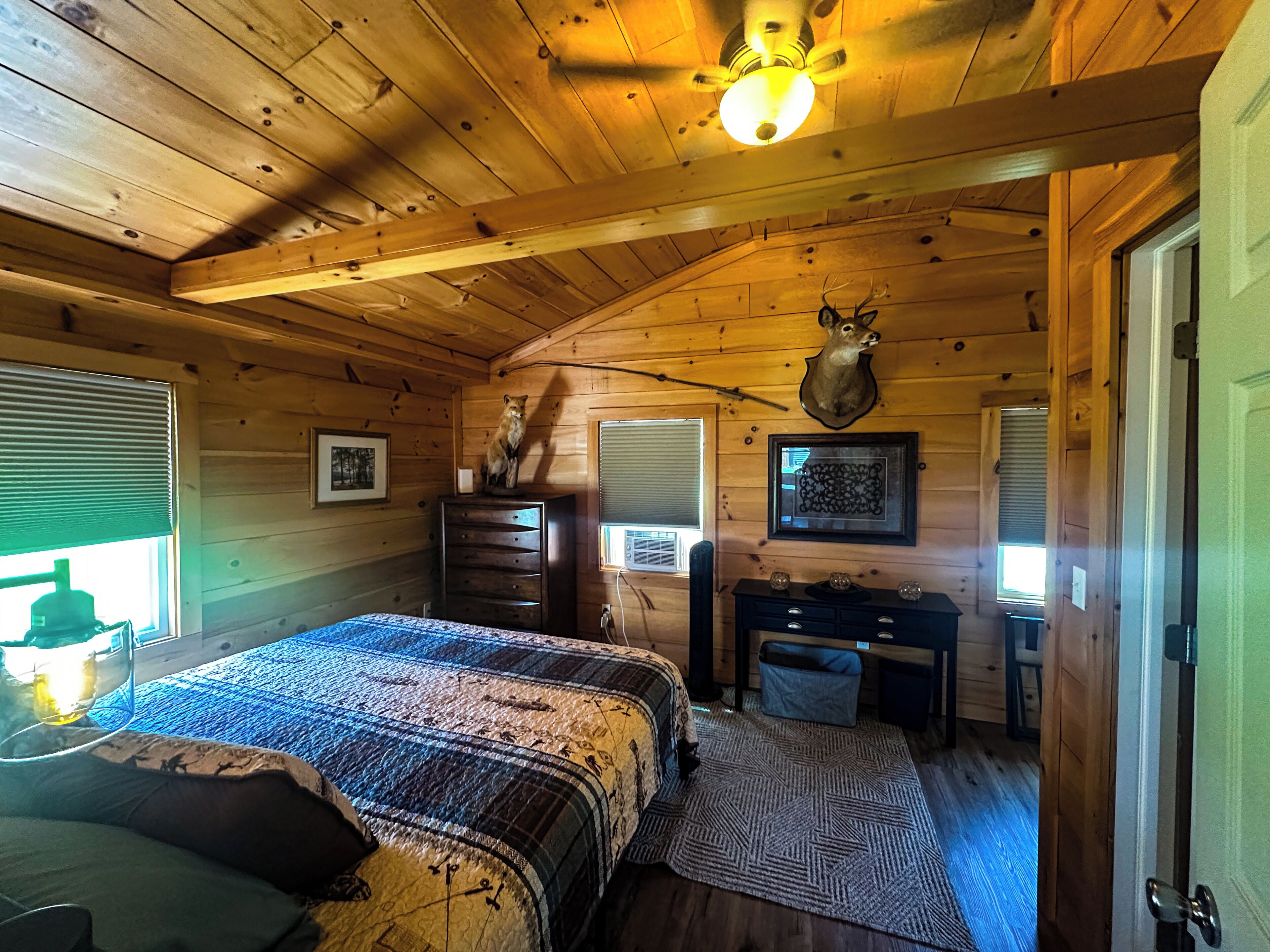 A log cabin bedroom with a bed, dresser, desk, and a mounted deer head.