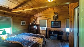 A log cabin bedroom with a bed, dresser, desk, and a mounted deer head.