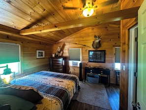 A log cabin bedroom with a bed, dresser, desk, and a mounted deer head.
