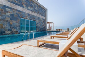 A poolside area with lounge chairs, a glass door, and a view of the sea. - Palmetto Beach - ILLUMINATO (Cartagena)