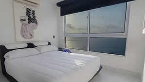 A bedroom with a large bed, a window with a view, and a wall art piece. - Palmetto Beach - ILLUMINATO (Cartagena)