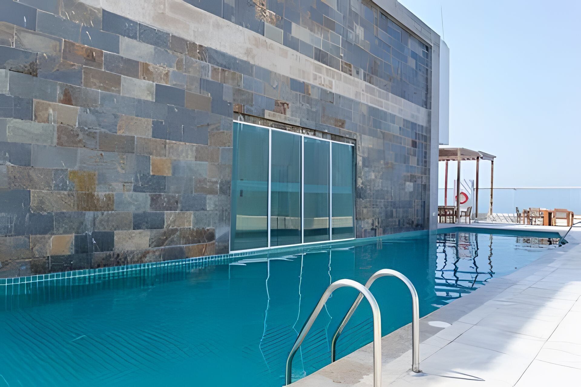 A swimming pool with a glass wall, a covered seating area, and a view of the sea.
