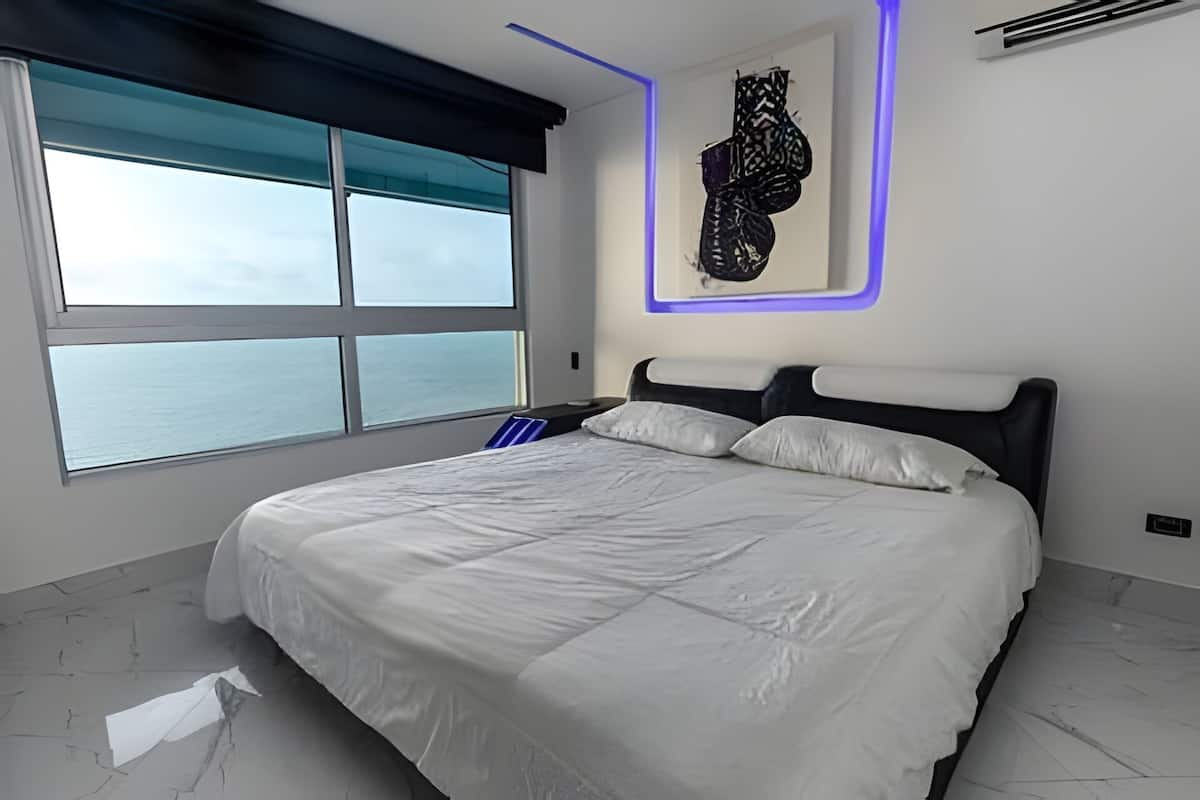 A bedroom with a large bed, a view of the sea, and a modern wall design.