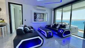 A modern living room with a large window, a flat-screen TV, and a seating area with massage chairs. - Palmetto Beach - ILLUMINATO (Cartagena)