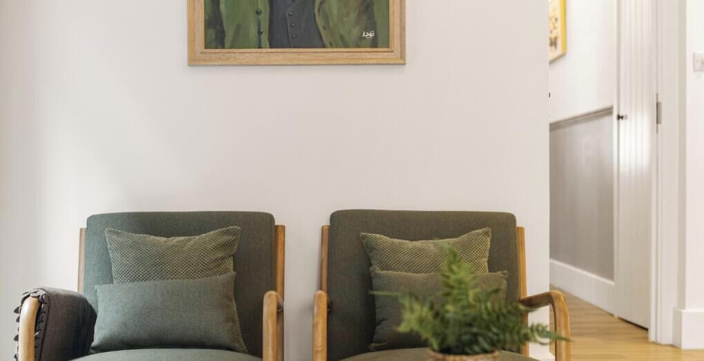 Two armchairs with cushions, a small table with a plant, and a door in the background.