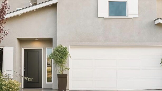 Une maison moderne à deux étages, dotée d’un garage, d’une porte d’entrée et d’un petit jardin agrémenté de plantes et d’un sentier.