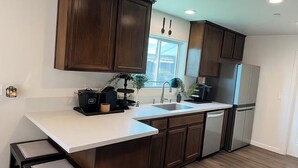Une cuisine moderne avec des meubles de couleur bois foncé, un plan de travail blanc, un réfrigérateur en acier inoxydable et une fenêtre offrant une belle vue.