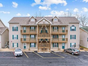 A multi-story building with a central staircase, balconies, and a parking lot with two cars. - Lake Taneycomo View -  Cozy 1BR Condo - Fireplace (Branson)