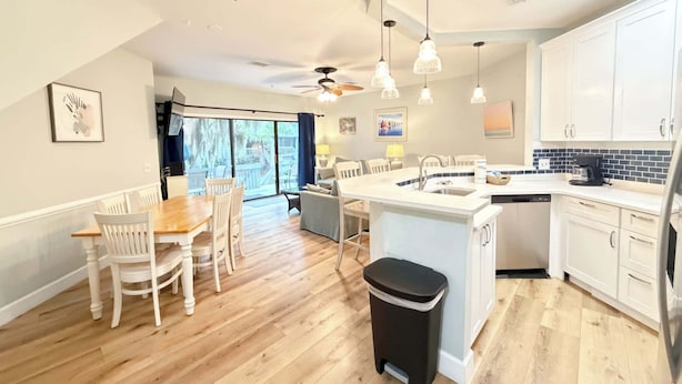 A spacious kitchen with a central island, white cabinetry, and a dining area with a wooden table and chairs. - Ocean Breeze - Walk to Beach 3BR Lagoon View Villa (Hilton Head Island)