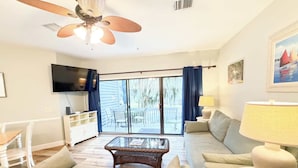 A living room with a ceiling fan, a flat-screen TV, a glass-top coffee table, and a sofa. - Ocean Breeze - Walk to Beach 3BR Lagoon View Villa (Hilton Head Island)