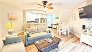 A living room with a sofa, coffee table, and TV. There is a kitchen in the background. - Ocean Breeze - Walk to Beach 3BR Lagoon View Villa (Hilton Head Island)