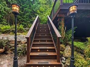 A wooden staircase with railings and lights, surrounded by greenery and rocks.