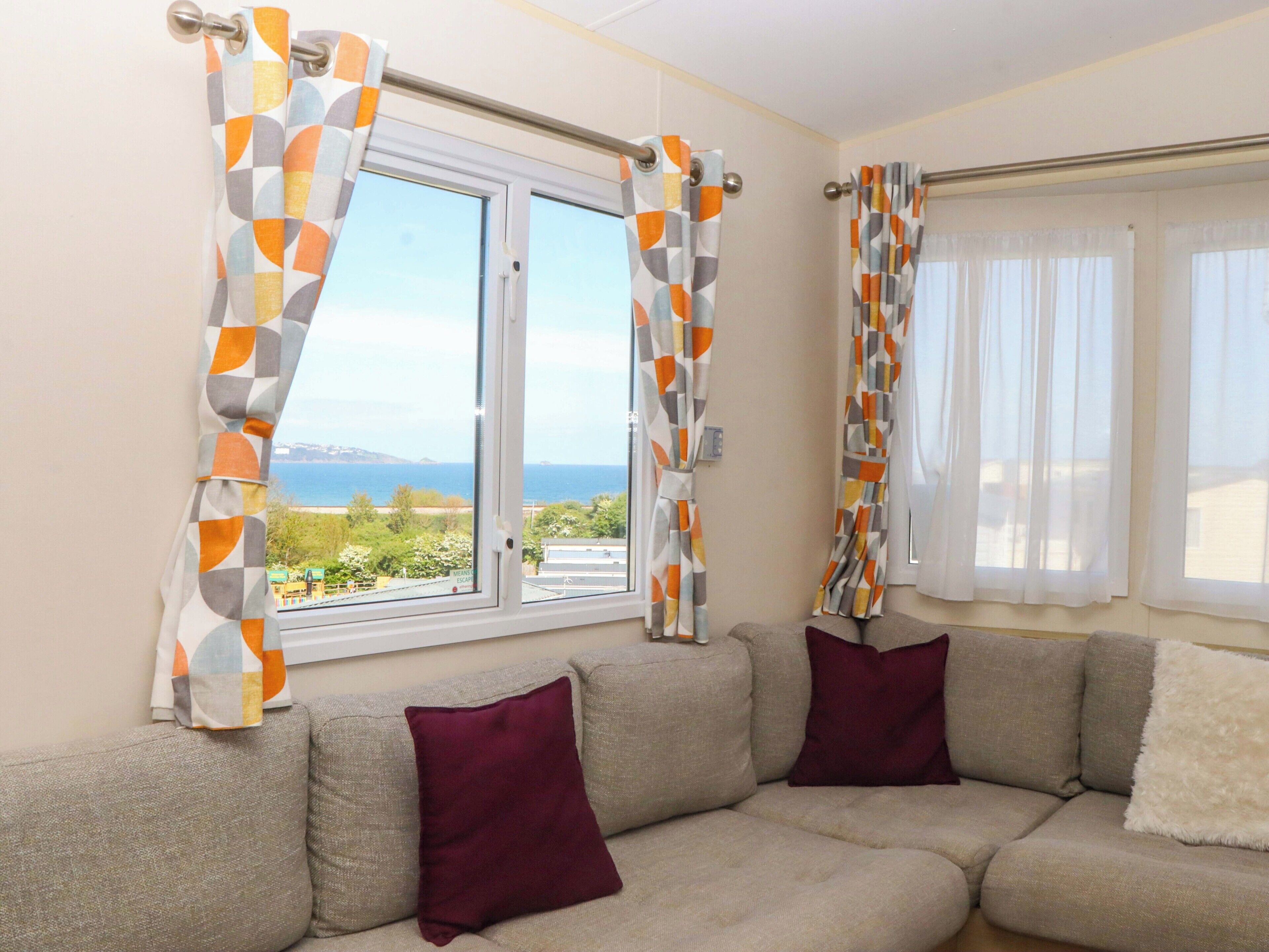 A living room with a sofa, two windows with curtains, and a view of the sea.