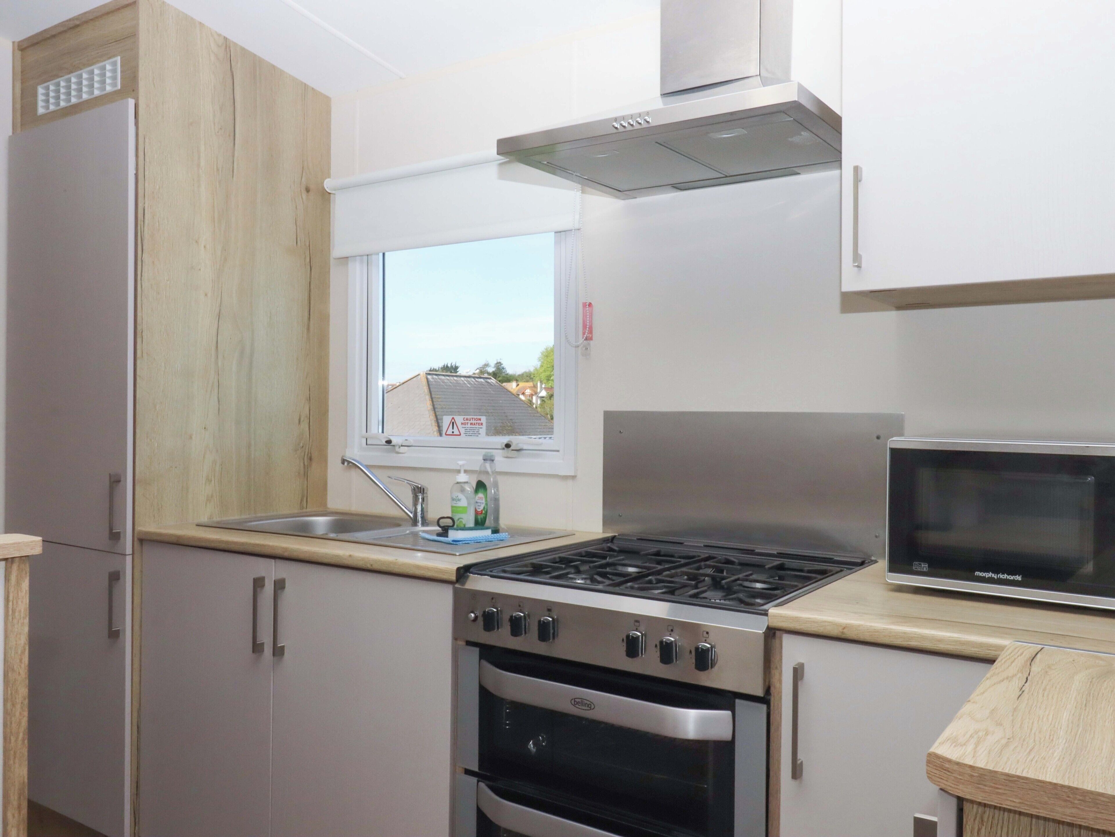 Une cuisine équipée d’une cuisinière, d’un four, d’un four à micro-ondes et d’une fenêtre donnant sur des maisons.