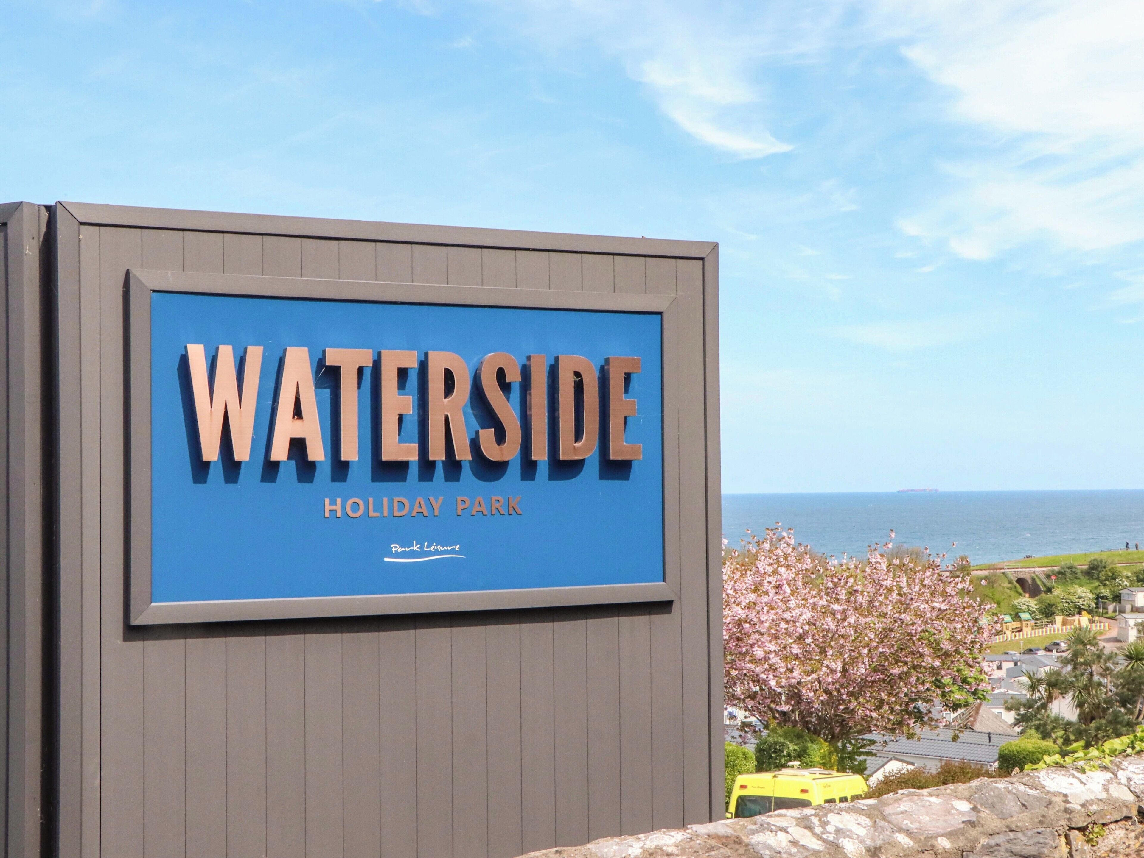 Indicador de Waterside Holiday Park amb vista al mar i flors de cirera.