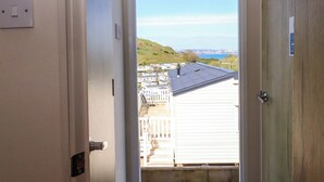 Una puerta que da a un balcón con vistas a una colina y edificios al fondo.