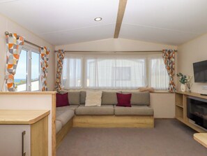 A cozy living room with a sofa, a television, and a window with curtains. - 213 Seaview Caravan (Paignton)