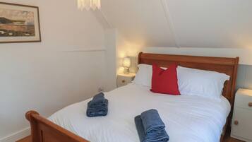 Ein Schlafzimmer mit einem hölzernen Bett, weißer Bettwäsche, einem roten Kopfkissen und zwei gerollten Handtüchern.