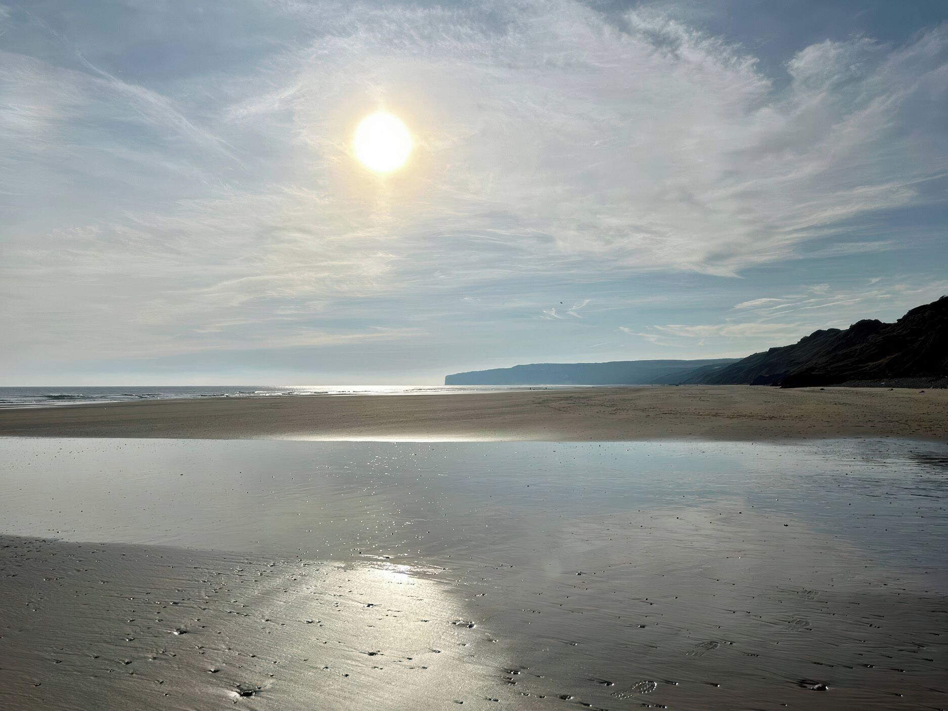 A beach with a calm sea, a clear sky, and distant hills.