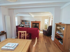 A living room with a red sofa, wooden table, and bookshelves. - Fleming Cottage (Filey)