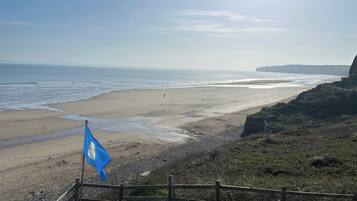 Blick auf die Küste mit einem Sandstrand, einem Holzzaun und einer Fahne.