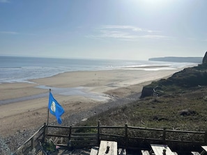 A coastal view with a sandy beach, a wooden fence, and a flag. - Fleming Cottage (Filey)