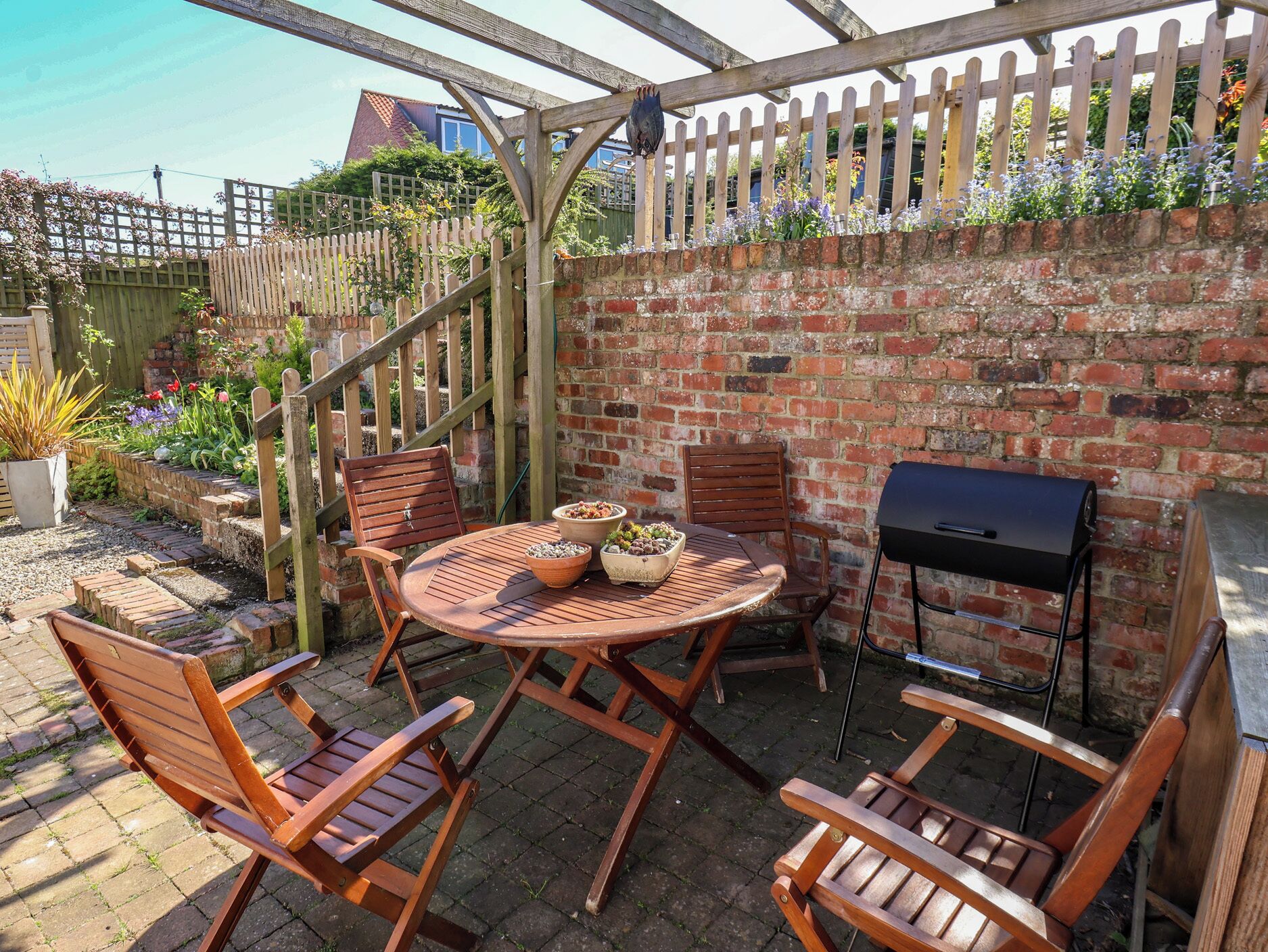 Eine Terrasse mit einem runden Tisch, zwei Holzstühlen, einem Grill und einer Holz-Pergola.