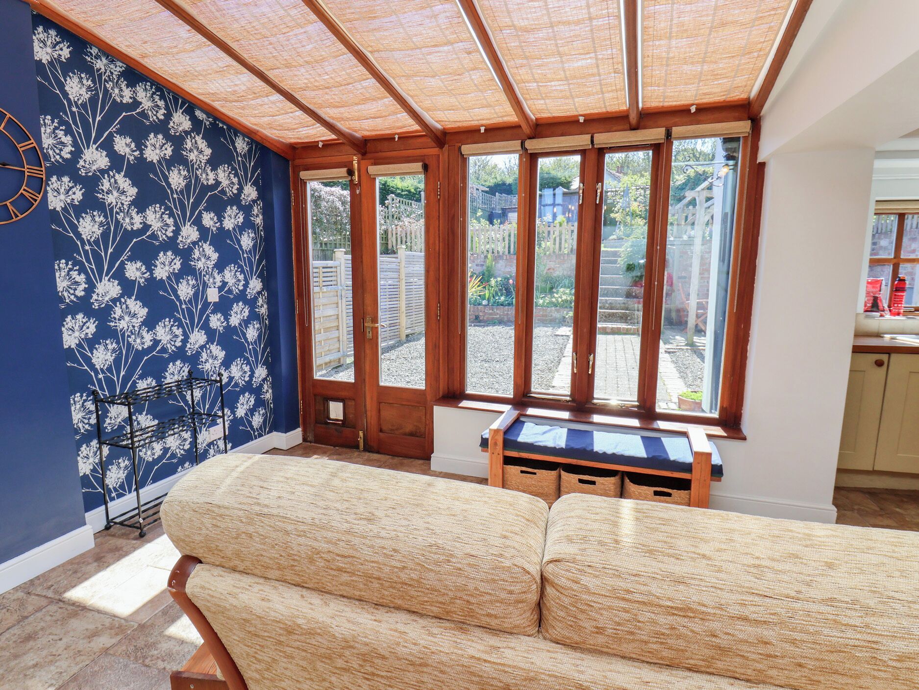 A room with a blue floral wall, a wooden bench, and a view through a glass door.