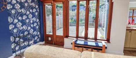 A room with a blue floral wall, a wooden bench, and a view through a glass door.