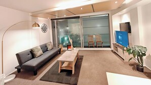 Een moderne woonkamer met een bank, salontafel, televisie en glazen schuifdeuren die uitkomen op een balkon.