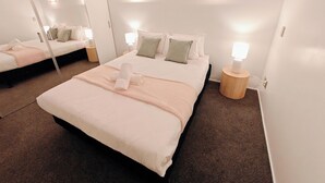 Een hotelkamer met een groot bed, een nachtkastje met een lamp en een spiegel.