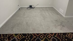 A room with a carpeted floor, white walls, a ceiling light, and a power strip on the floor.