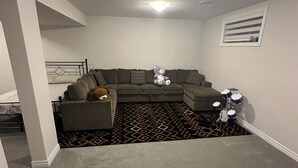 A living room with a sectional sofa, a patterned rug, and a drum set.