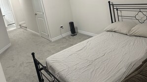A bedroom with a bed, a carpeted floor, a white door, and a hallway leading to another room.